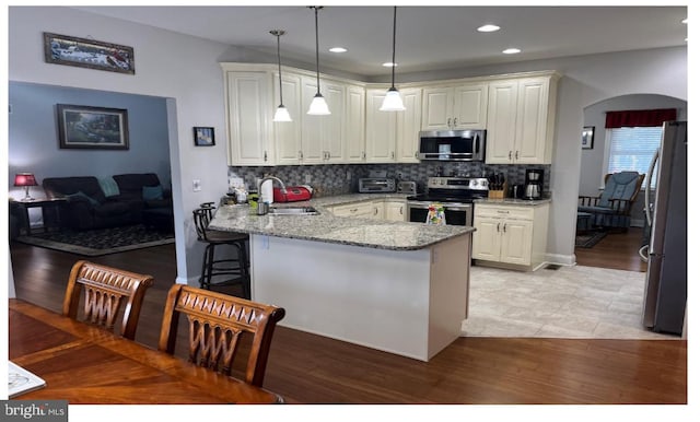 kitchen with light hardwood / wood-style flooring, kitchen peninsula, stainless steel appliances, sink, and a breakfast bar