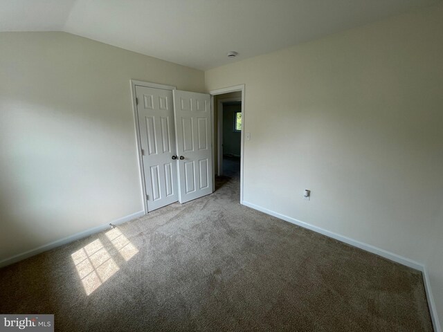 unfurnished bedroom featuring carpet floors, lofted ceiling, and a closet