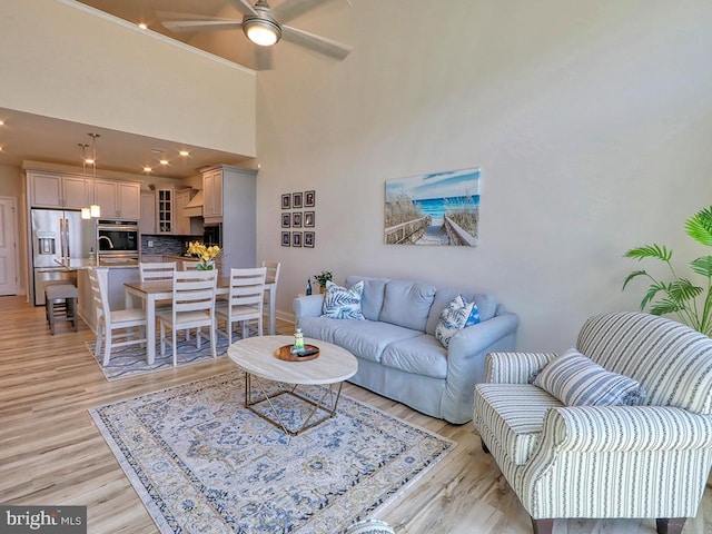 living room with light hardwood / wood-style floors, a high ceiling, and ceiling fan