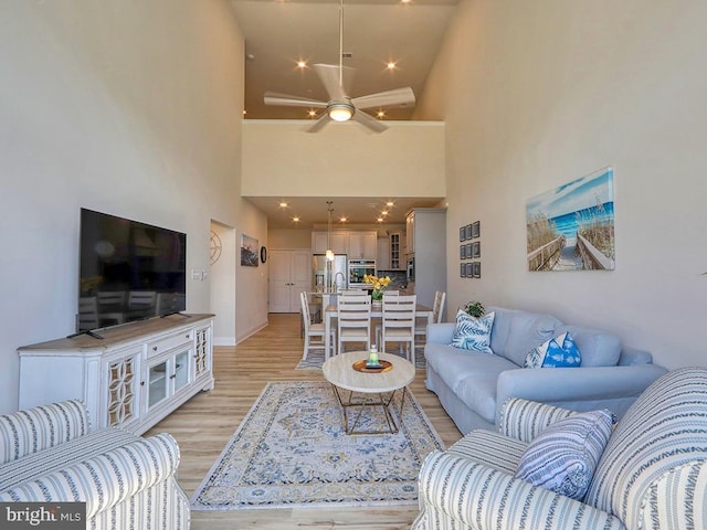 living room featuring light wood-style flooring, a high ceiling, a ceiling fan, and recessed lighting