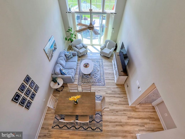 living room featuring ceiling fan, a towering ceiling, light hardwood / wood-style flooring, and a healthy amount of sunlight