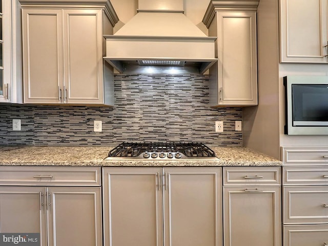 kitchen with decorative backsplash, stainless steel gas cooktop, premium range hood, and light stone counters