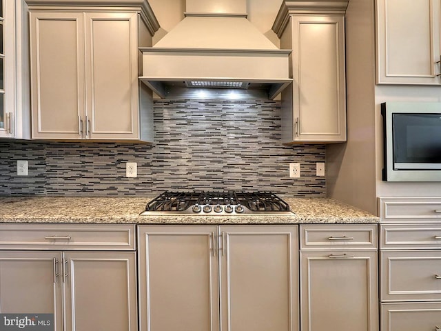 kitchen with stainless steel gas stovetop, custom exhaust hood, backsplash, and light stone counters