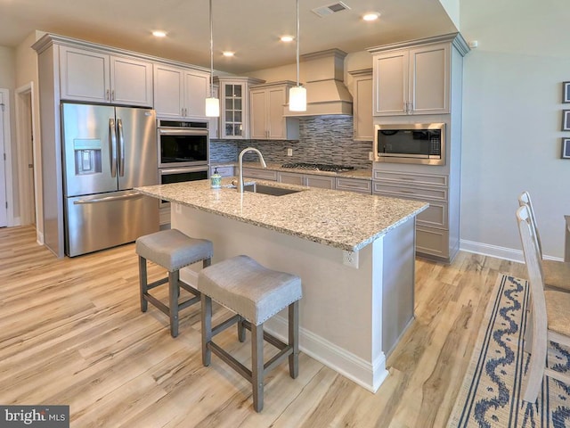 kitchen with light hardwood / wood-style flooring, tasteful backsplash, custom exhaust hood, sink, and stainless steel appliances