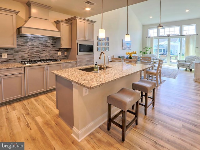 kitchen with custom range hood, light hardwood / wood-style flooring, a center island with sink, and stainless steel gas stovetop