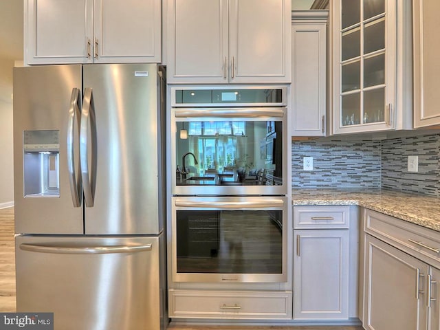 kitchen with hardwood / wood-style flooring, backsplash, appliances with stainless steel finishes, and light stone countertops