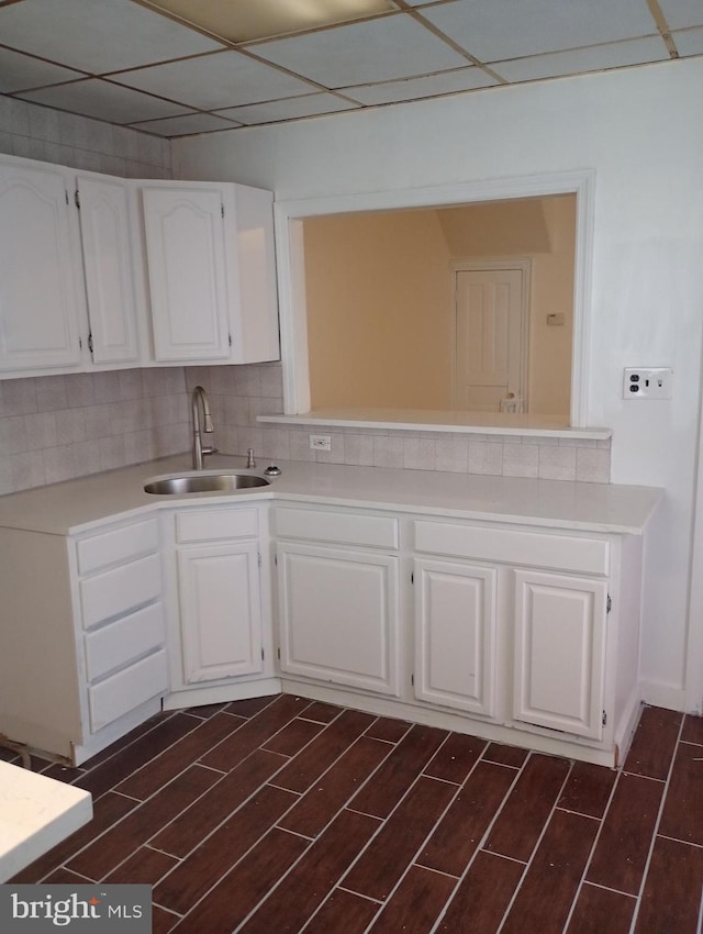 kitchen with white cabinets, decorative backsplash, sink, and a drop ceiling