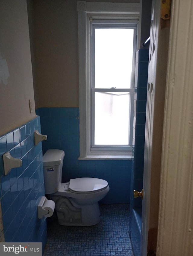 bathroom featuring toilet, a healthy amount of sunlight, tile patterned floors, and tile walls