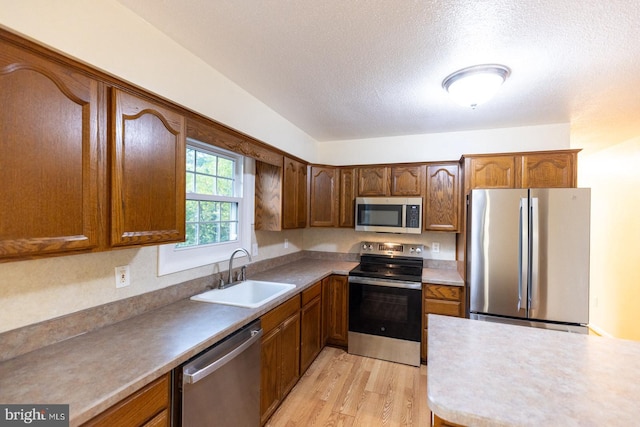 kitchen featuring light wood-type flooring, a textured ceiling, appliances with stainless steel finishes, and sink