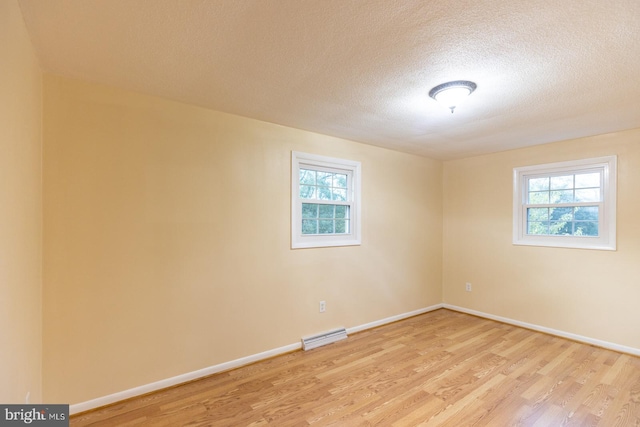 empty room with light wood-type flooring and a textured ceiling