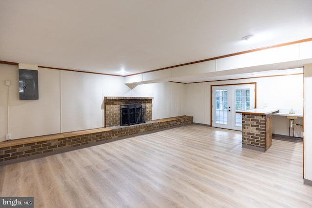 unfurnished living room featuring a brick fireplace, light wood-type flooring, crown molding, french doors, and electric panel