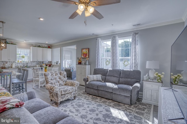 living room featuring ceiling fan, ornamental molding, and light wood-type flooring