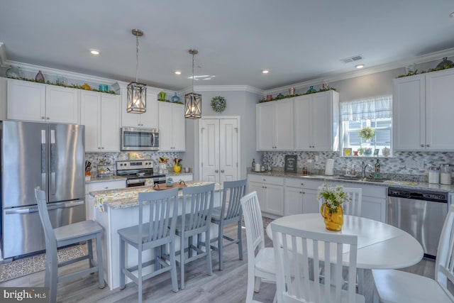 kitchen featuring backsplash, appliances with stainless steel finishes, light hardwood / wood-style flooring, a kitchen island, and pendant lighting