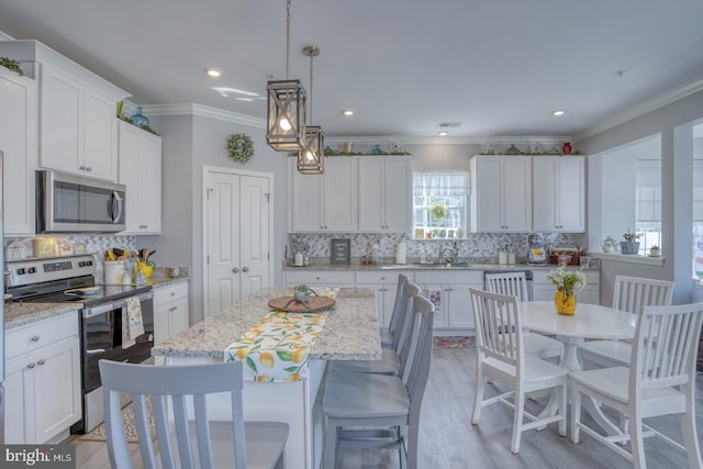 kitchen with appliances with stainless steel finishes, backsplash, light hardwood / wood-style floors, white cabinets, and a center island