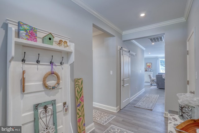 mudroom with a barn door, wood finished floors, visible vents, baseboards, and crown molding