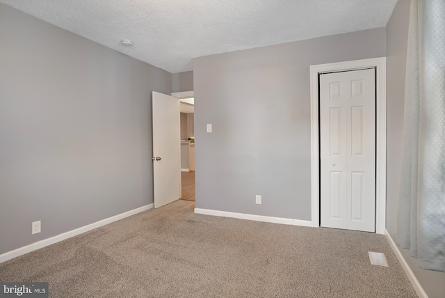 unfurnished bedroom with carpet floors, a closet, a textured ceiling, and baseboards