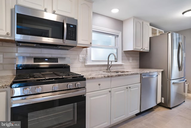 kitchen with tasteful backsplash, white cabinets, appliances with stainless steel finishes, light stone countertops, and a sink