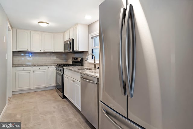 kitchen featuring appliances with stainless steel finishes, white cabinets, a sink, and light stone countertops