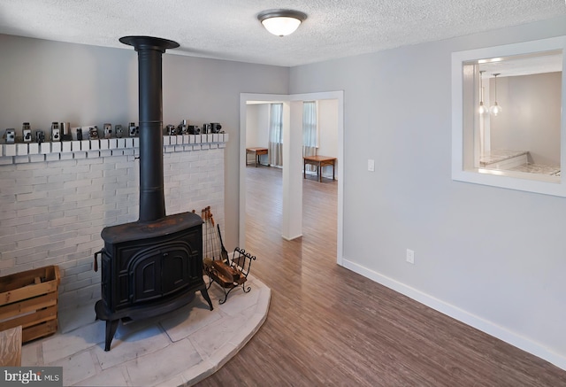 interior details featuring a wood stove, a textured ceiling, baseboards, and wood finished floors