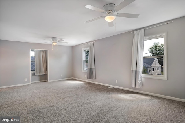 carpeted spare room featuring a wealth of natural light, ceiling fan, and baseboards