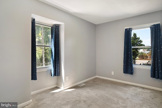 carpeted empty room with plenty of natural light, visible vents, and baseboards