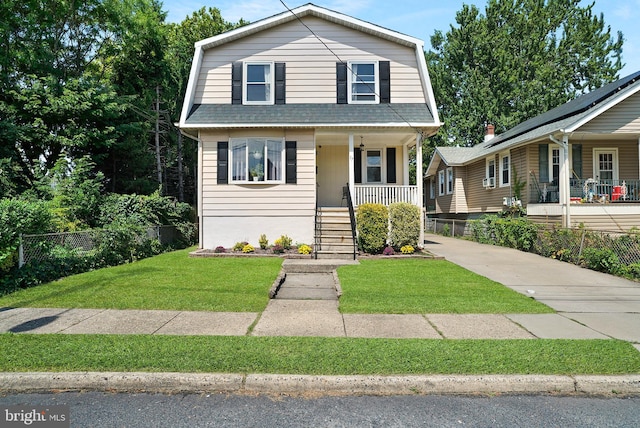 dutch colonial with a gambrel roof, roof with shingles, covered porch, fence, and a front lawn