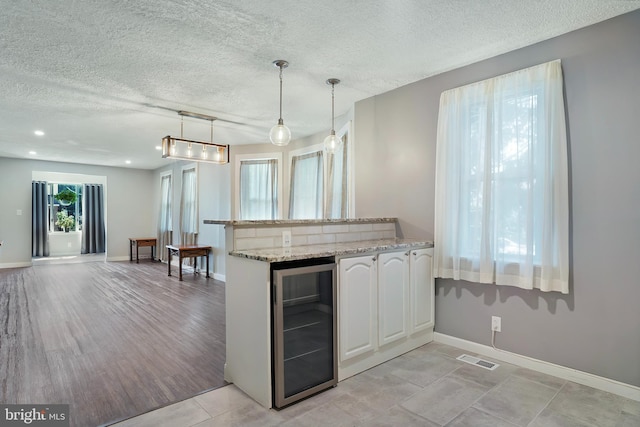 kitchen with wine cooler, white cabinets, open floor plan, light stone countertops, and decorative light fixtures