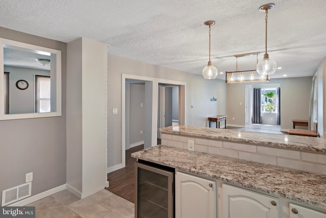 kitchen with decorative light fixtures, visible vents, white cabinetry, a textured ceiling, and beverage cooler