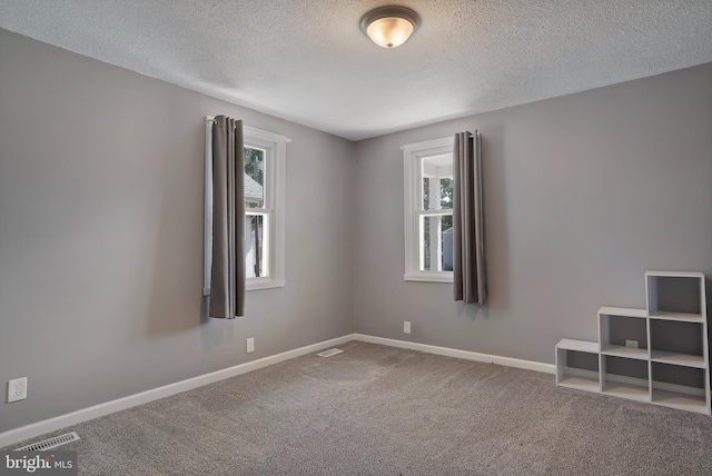 empty room with carpet floors, visible vents, a textured ceiling, and baseboards