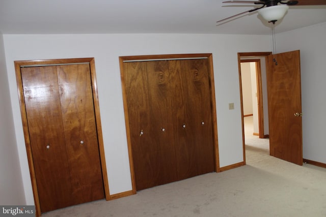 unfurnished bedroom with light colored carpet, two closets, and ceiling fan