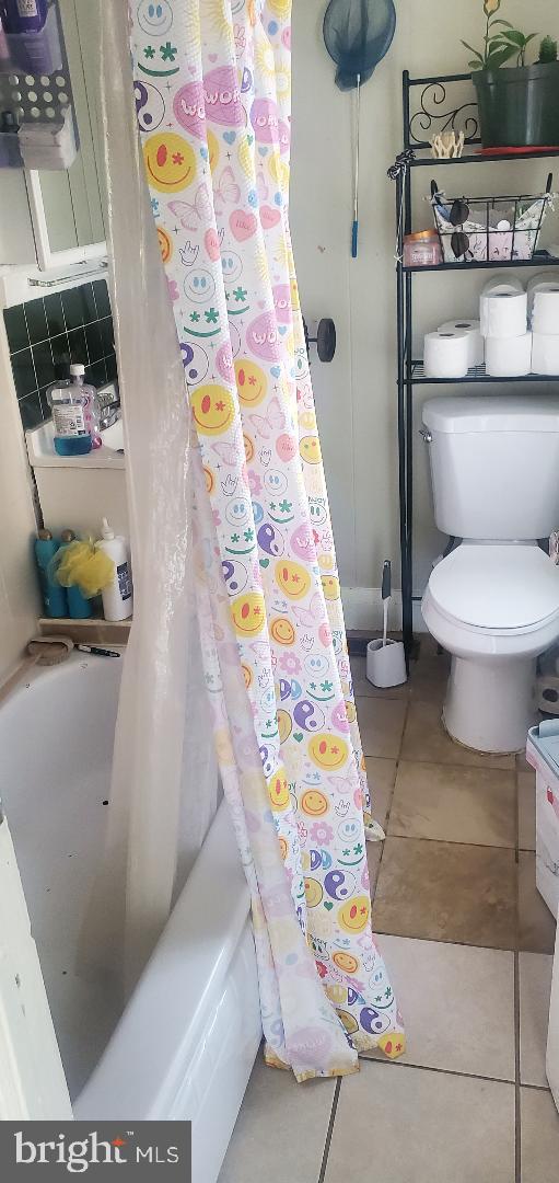 bathroom featuring tile patterned flooring, toilet, and shower / bath combo with shower curtain