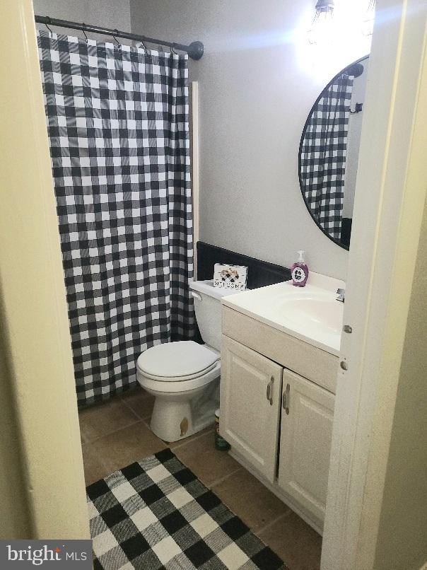 bathroom with a shower with curtain, vanity, toilet, and tile patterned floors