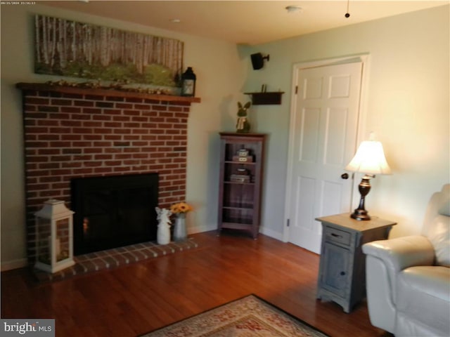 living area featuring a brick fireplace, baseboards, and wood finished floors