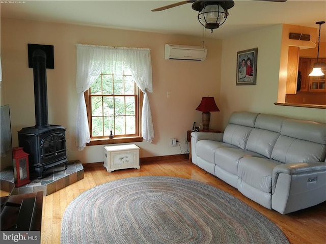 living room with light wood-style flooring, a wall mounted AC, a ceiling fan, a wood stove, and baseboards