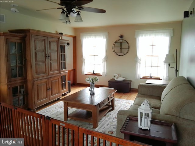 living room featuring light wood-style floors, ceiling fan, visible vents, and baseboards