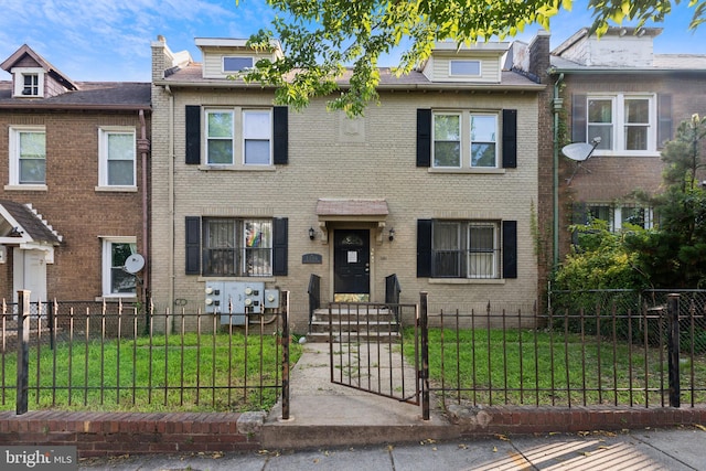 view of property with brick siding, a fenced front yard, a front yard, and a gate