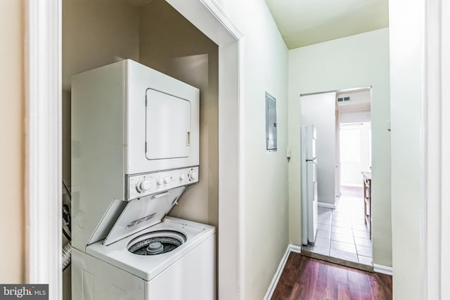 laundry room featuring laundry area, baseboards, electric panel, dark wood-style floors, and stacked washer and clothes dryer