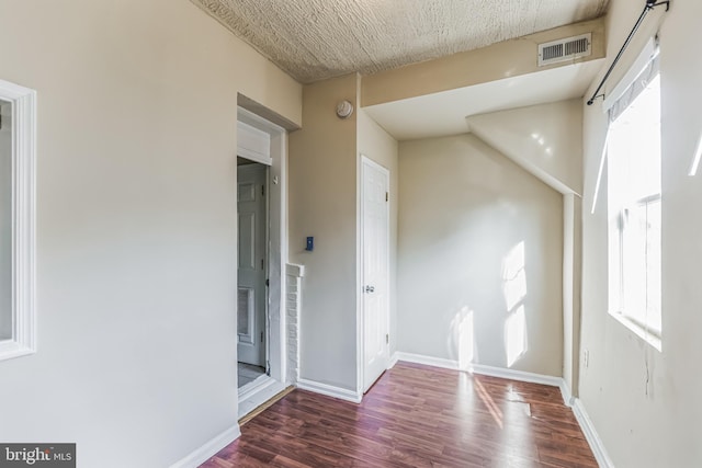 empty room featuring a textured ceiling, dark wood-type flooring, visible vents, and baseboards