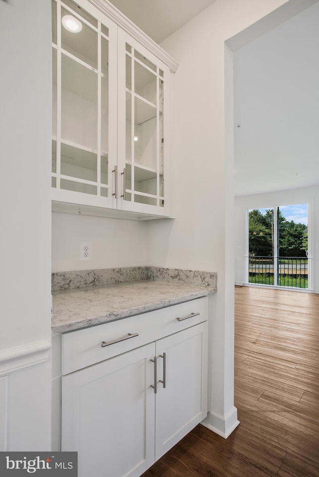 bar with dark hardwood / wood-style floors, light stone counters, and white cabinets