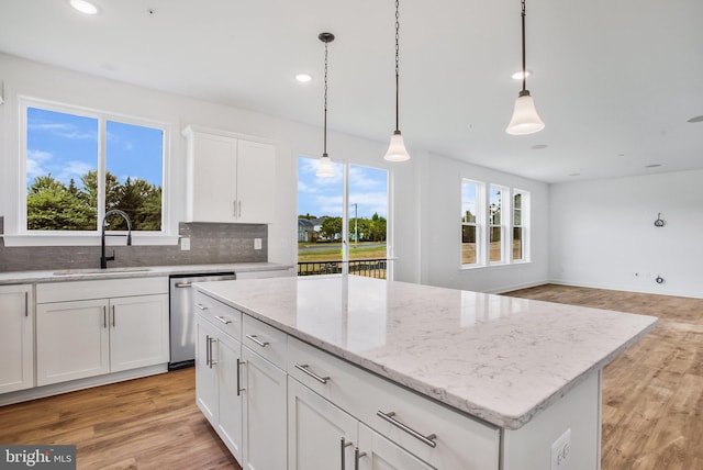 kitchen with backsplash, sink, light hardwood / wood-style floors, stainless steel dishwasher, and white cabinets