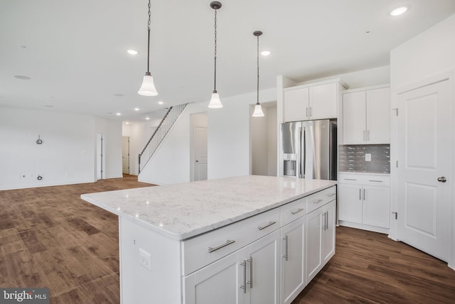 kitchen with decorative backsplash, light stone counters, a kitchen island, stainless steel fridge, and dark wood-type flooring