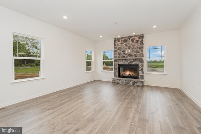 unfurnished living room with plenty of natural light, light hardwood / wood-style flooring, and a stone fireplace