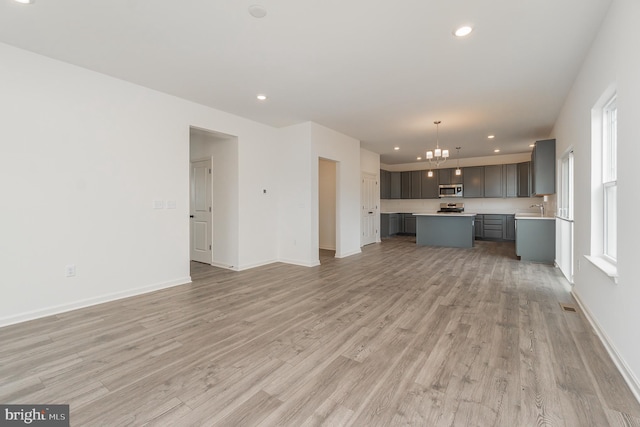 unfurnished living room with sink, light hardwood / wood-style floors, and an inviting chandelier