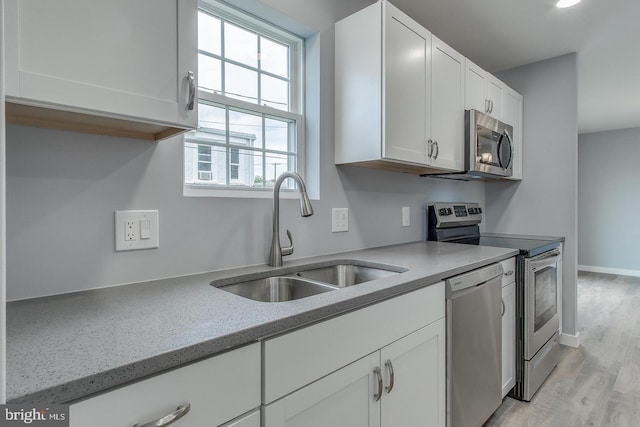 kitchen with light hardwood / wood-style flooring, stainless steel appliances, sink, light stone countertops, and white cabinets