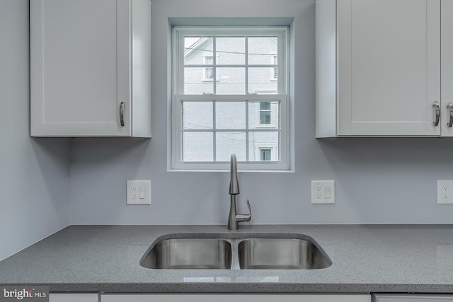 kitchen with sink, light stone counters, and white cabinets