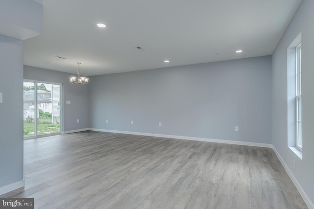 unfurnished room featuring light wood-type flooring, plenty of natural light, and a chandelier