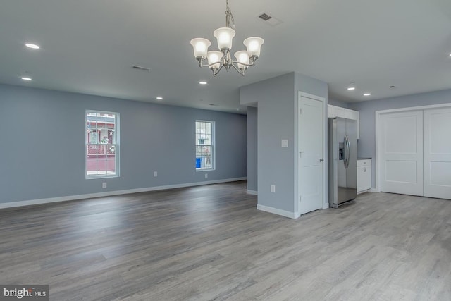 unfurnished living room with an inviting chandelier, light hardwood / wood-style flooring, and a healthy amount of sunlight