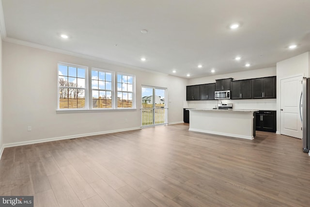 kitchen with a center island with sink, appliances with stainless steel finishes, open floor plan, dark cabinets, and wood finished floors