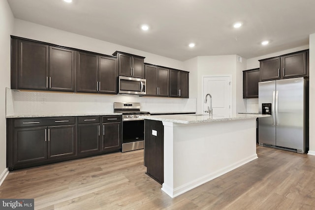 kitchen with light wood-style flooring, a kitchen island with sink, stainless steel appliances, a sink, and dark brown cabinets