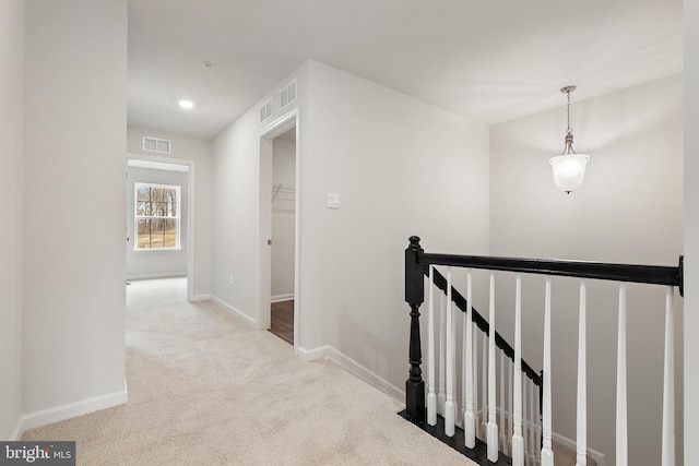 corridor with visible vents, baseboards, an upstairs landing, and light colored carpet